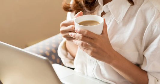 Person holding a cup of coffee while working on a laptop, exploring if they can take NMN with coffee